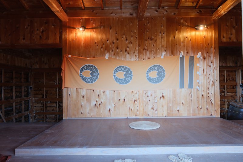 城跡の小屋の中。木の梁と、紋の入った幕。